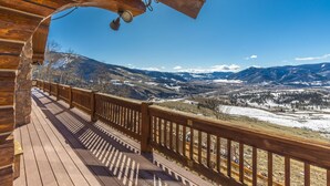 Eine Holzterrasse mit Blick auf verschneite Berge und ein Tal.