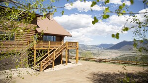 Eine Blockhütte mit einer Holzterrasse und einer Treppe zu einem Balkon im zweiten Stock.
