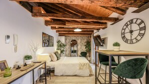 Une chambre avec un plafond en bois, une grande horloge murale, un lit, un bureau et deux chaises.