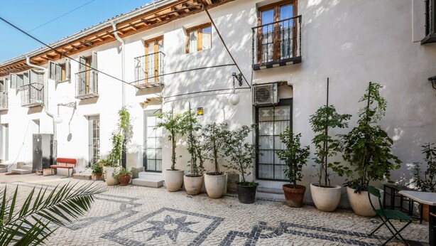 Une cour avec un sol carrelé, des plantes en pot et des sièges d’extérieur.