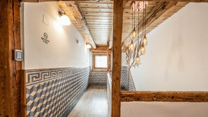 Un couloir aux murs ornés de motifs, avec des poutres en bois et des luminaires suspendus.