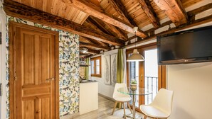 A room with wooden beams, a wooden door, a kitchen area with a sink, two white chairs, a glass table, and a TV mounted on the wall. - Beautiful Renovated Loft in the center 010  (Madrid)