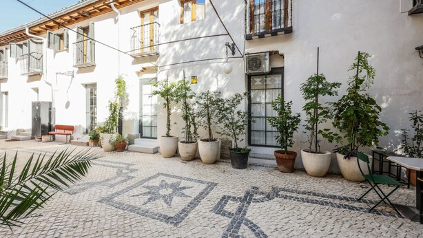 A courtyard with tiled flooring, potted plants, outdoor seating, and a building with balconies and windows. - Beautiful Renovated Loft in the center 010  (Madrid)