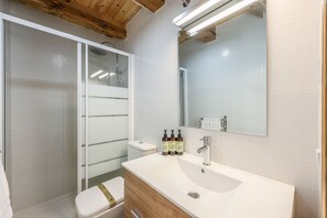 A bathroom with a white sink, wooden vanity, a glass shower enclosure, and a mirror above the sink. - Beautiful Renovated Loft in the center 9  (Madrid)