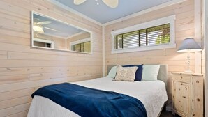 A bedroom with a bed, a nightstand, a mirror, and a window with blinds.