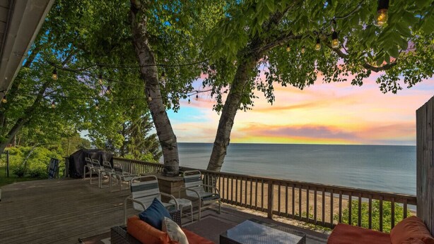A wooden deck with outdoor furniture, overlooking a body of water at sunset.