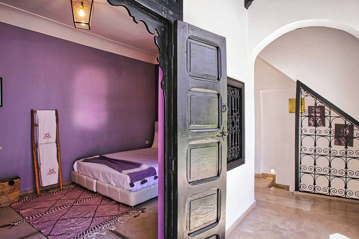 Un dormitorio con cama, una lámpara colgante, una puerta con reja metálica decorativa y una escalera con barandilla de metal.
