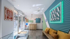 Eine Hotelhalle mit einer Rezeption, einer gepolsterten Bank, einer Treppe und einem Schild mit der Aufschrift 'AMA ZINN places'.