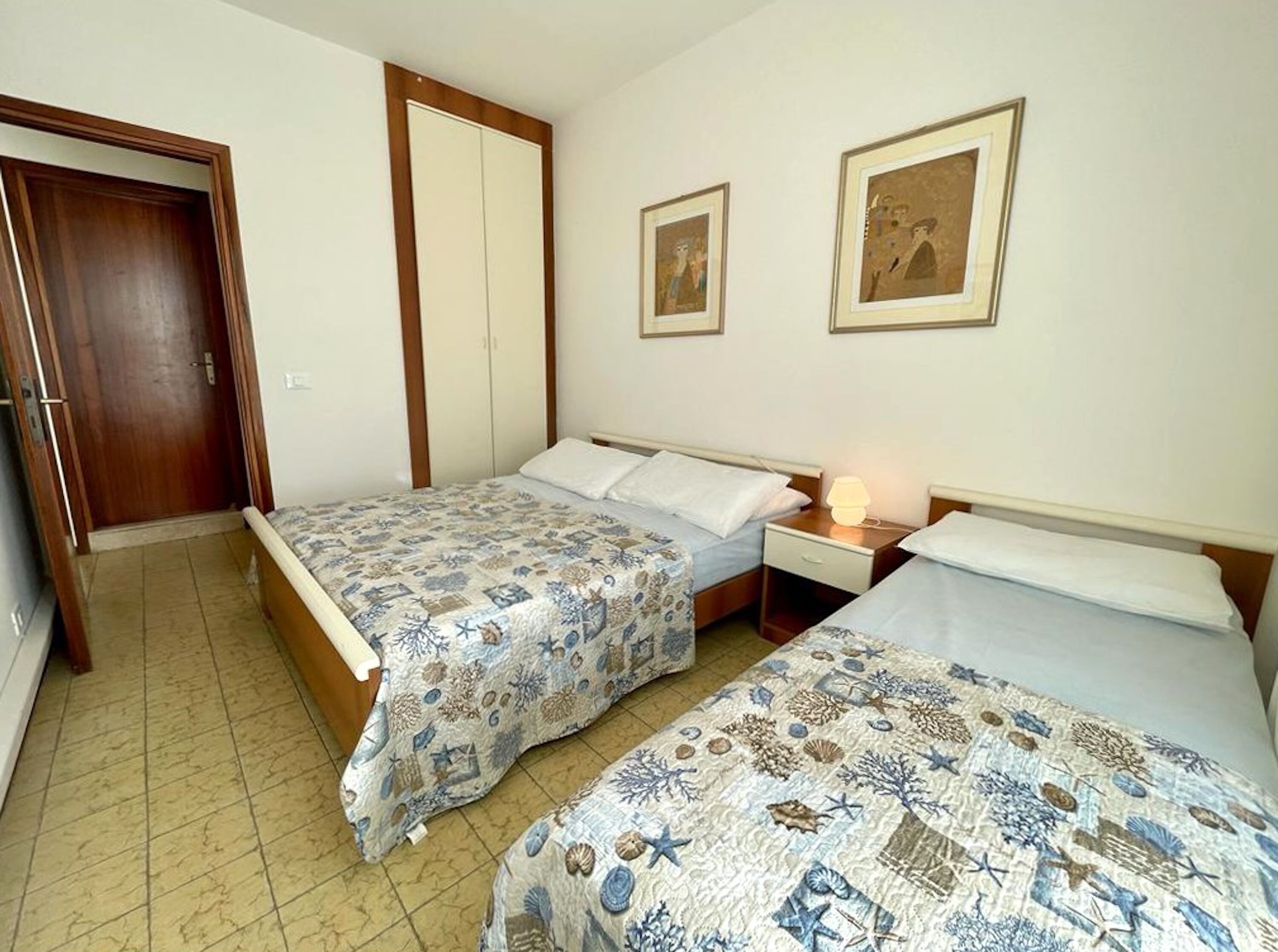 Une chambre avec deux lits, une armoire et deux tableaux encadrés au mur.