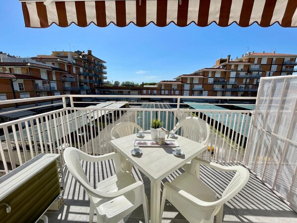 Un balcón con mesa y sillas, un toldo a rayas y vistas a edificios residenciales.