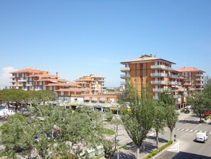 Un edificio residencial de varios pisos con balcones, un estacionamiento y árboles en primer plano.