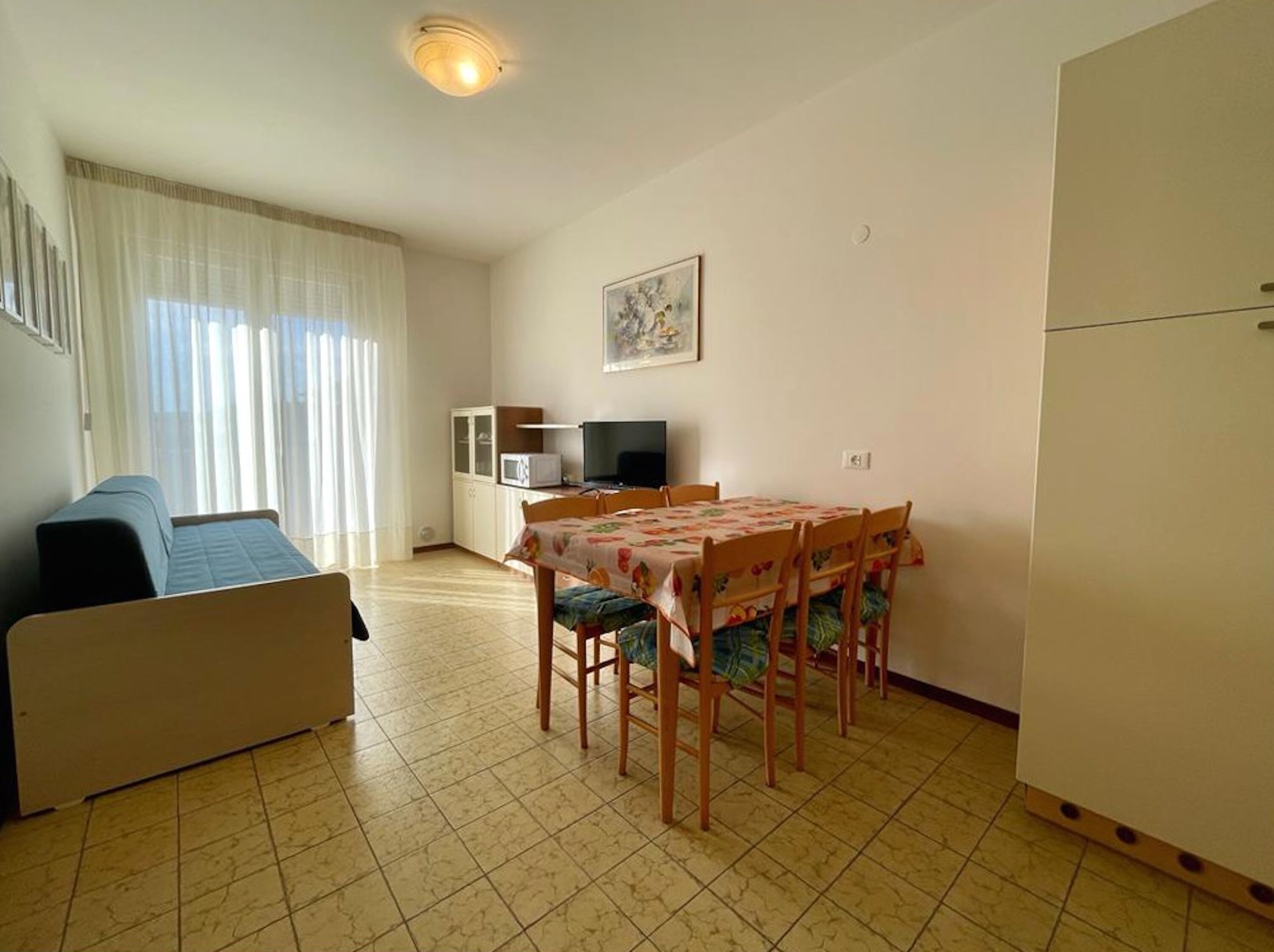 Un espace de vie compact comprenant un canapé, une table à manger, des chaises, un téléviseur et un réfrigérateur.