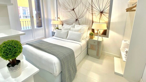 A modern bedroom with a bed, bedside tables, a lamp, and a view of the outside. - Design apartment in Plaza Mayor 2 I (Madrid)
