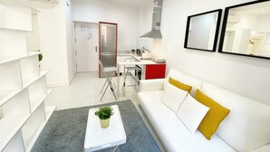 A modern living room with a white sofa, a coffee table with a plant, and a kitchen area in the background. - Design apartment in Plaza Mayor 2 I (Madrid)