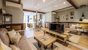 A modern living room with a sofa, coffee table, TV, and a kitchen in the background. - Design loft in CHUECA I3IZQ (Madrid)