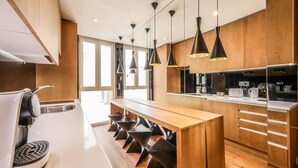 A modern kitchen with a long island, black pendant lights, wooden cabinets, and a built-in oven. - Design loft in CHUECA I3IZQ (Madrid)