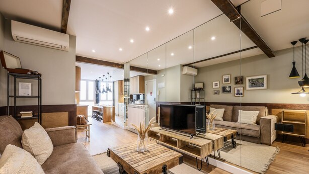 A modern living room with a sofa, coffee table, TV, and a kitchen in the background. - Design loft in CHUECA I2IZQ (Madrid)