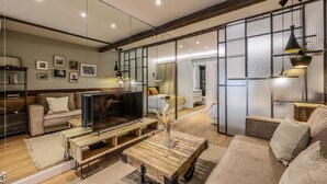 A modern living room with a sofa, coffee table, TV, and a large mirror reflecting the room. - Design loft in CHUECA I2IZQ (Madrid)