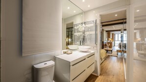 A modern bathroom with a large mirror, a white sink, and a wooden floor. - Design loft in CHUECA I2IZQ (Madrid)