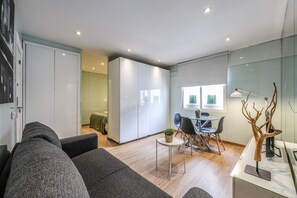 Un salon moderne avec un canapé gris, un coin repas avec une table et des chaises, et une cuisine équipée d’éléments de rangement.