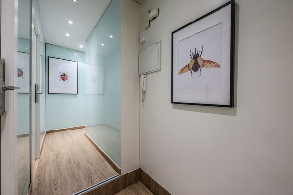 Un couloir aux murs ornés de tableaux encadrés, avec une porte en verre et un plancher en bois.