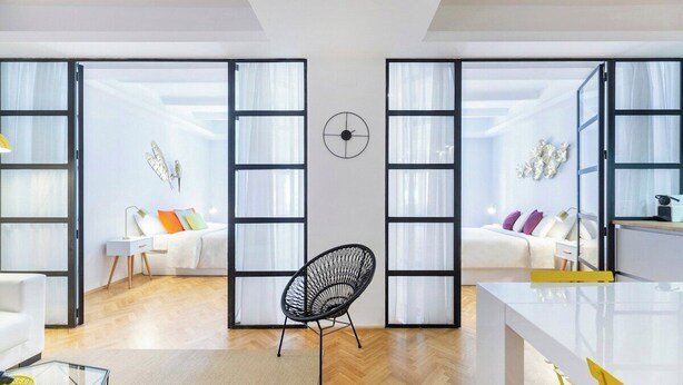 Una sala moderna con una butaca de estructura metálica negra, un sofá blanco y un escritorio blanco con una silla amarilla.