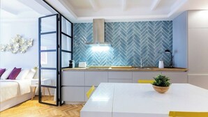 Una cocina moderna con salpicadero de baldosas en espiga, estufa integrada y una mesa de comedor blanca con sillas amarillas.
