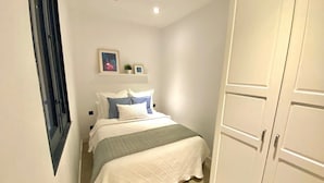 A bedroom with a bed, bedside tables, a nightstand, a wardrobe, and a small shelf with decorative items. - Incredible apartment in Atocha, 1C (Madrid)