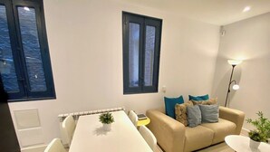 A modern living room with a white dining table, beige sofa, and a small round table with a plant. - Incredible apartment in Atocha, 1C (Madrid)