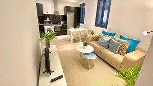 A modern living room with a sofa, coffee table, and TV. A kitchen is visible in the background. - Incredible apartment in Atocha, 1C (Madrid)