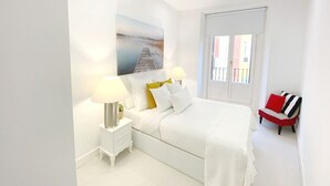 Une chambre moderne avec un lit, des tables de chevet, un fauteuil rouge et une fenêtre.