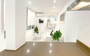 Ein modernes Interieur mit Küchenbereich, Esstisch mit Stühlen und einer kleinen Sitzecke mit Sofa und Pflanze.