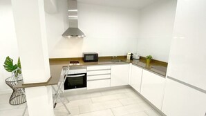 A modern kitchen with white cabinets, a stainless steel range hood, a microwave, and a sink. - Design apartment in Plaza Mayor 3D (Madrid)