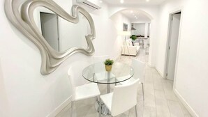 A modern dining area with a glass table and white chairs, a heart-shaped mirror, and a small plant on the table. - Design apartment in Plaza Mayor 3D (Madrid)