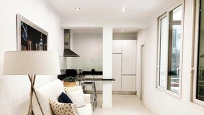 A modern living room with a white sofa, a floor lamp, and a kitchen area in the background. - Design apartment in Plaza Mayor 3D (Madrid)