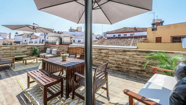 A rooftop terrace with wooden furniture, large umbrellas, and a view of the cityscape. - Penthouse with solarium  in Plaza Mayor and Sol (Madrid)