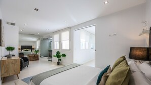 A modern bedroom with a large bed, a desk, and a TV. There are plants and a mirror on the walls. - Penthouse with solarium  in Plaza Mayor and Sol (Madrid)