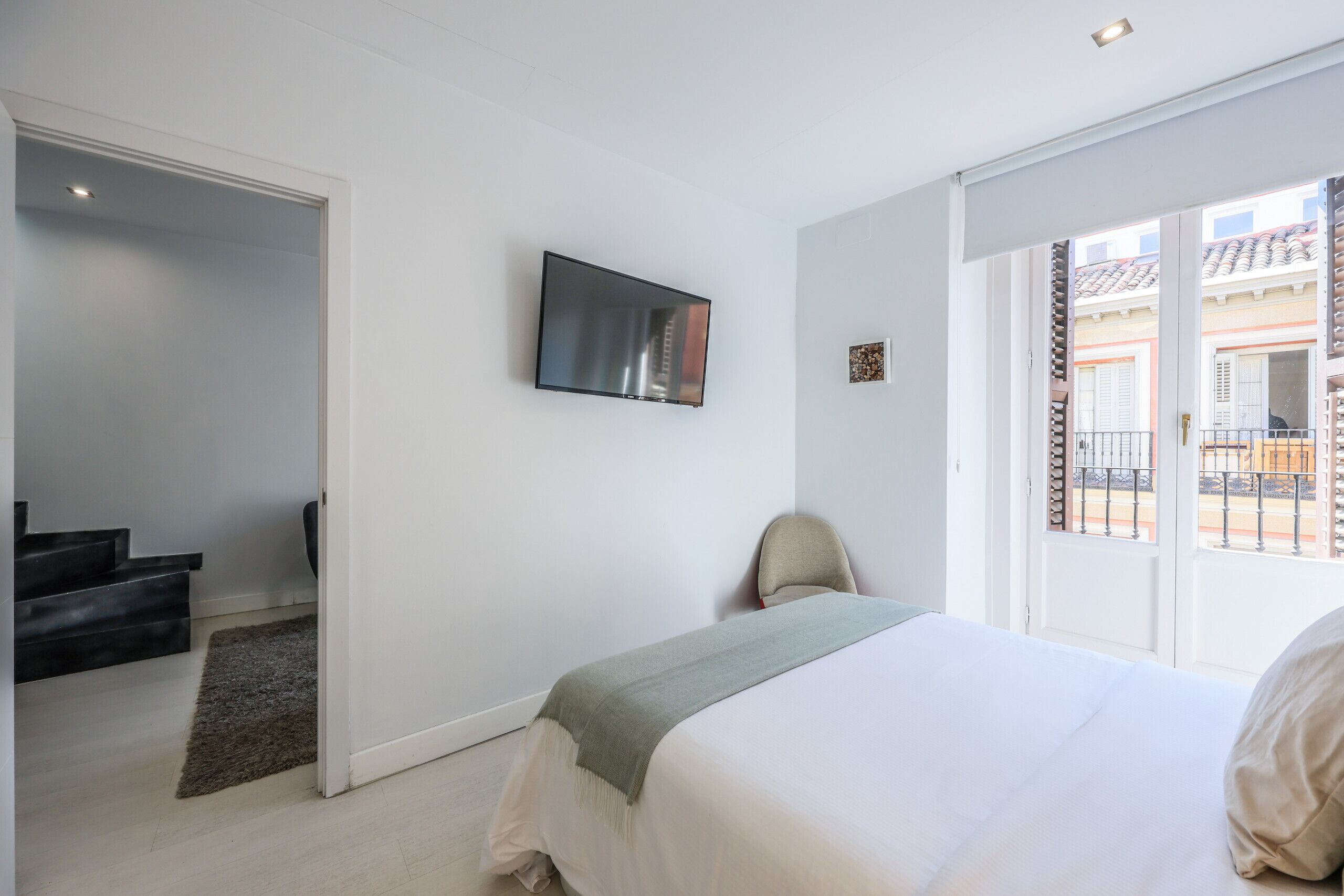 Un dormitorio con una cama, un televisor montado en la pared, una silla y vistas al balcón.