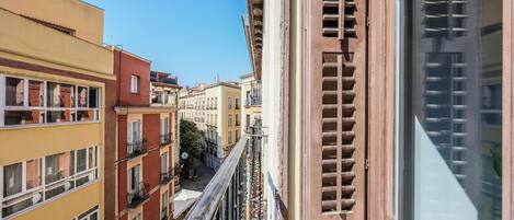 A narrow street with multi-story buildings, balconies, and a clear sky.