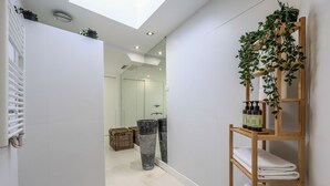 A modern bathroom with a skylight, a wooden shelf with towels, and a mirror reflecting the room. - Penthouse with solarium  in Plaza Mayor and Sol (Madrid)