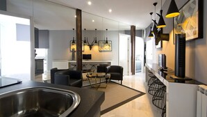A modern kitchen with a stainless steel sink, a dining area with a round table and chairs, and a living room with sofas and a fireplace. - Incredible design apartment 6C (Madrid)