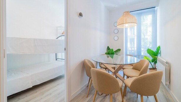 Une pièce moderne avec une table à manger en verre, quatre chaises, un luminaire suspendu et une fenêtre donnant sur un beau paysage.