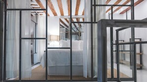 A modern hotel room with a large bed, a window with sheer curtains, and exposed wooden beams on the ceiling.