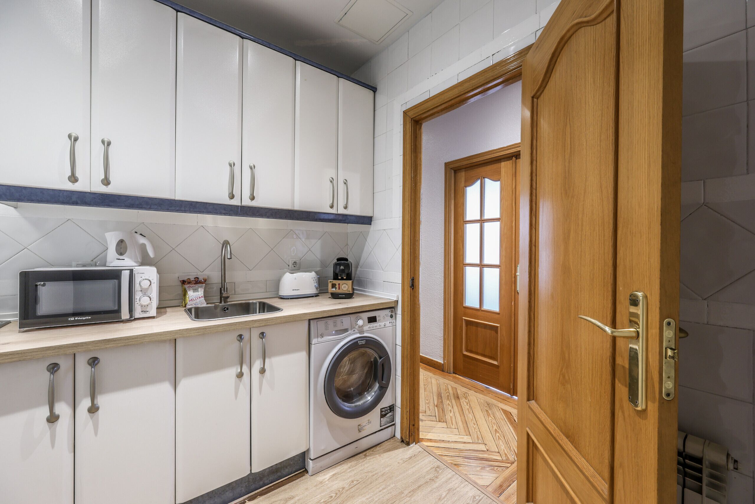 Une cuisine compacte avec des meubles blancs, un four à micro-ondes, un grille-pain et un lave-linge.