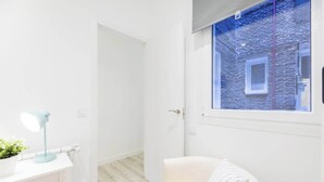 Une salle de bain moderne avec un meuble-lavabo blanc, une lampe bleue, une plante en pot et une vue sur un mur de briques à travers une fenêtre.