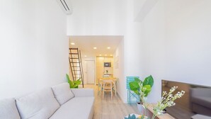 A modern living room with a sofa, a TV, and a dining area with a table and chairs.