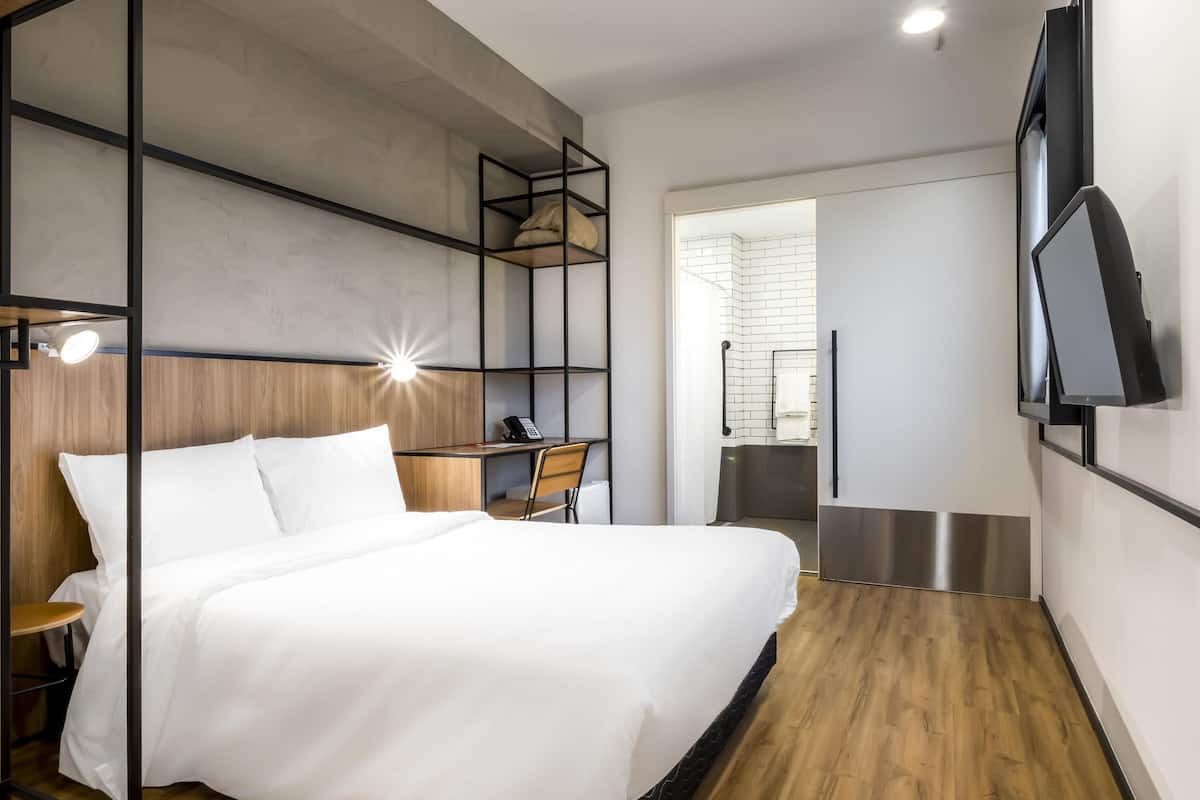 Habitación de hotel moderna con cama, escritorio, silla y televisor montado en la pared.