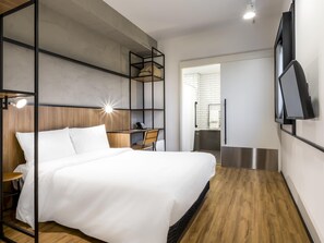 A modern hotel room with a bed, desk, chair, and a TV mounted on the wall. - Ibis Aruja (Aruja)