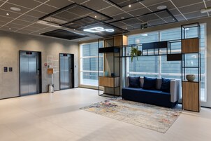 Um hall moderno com dois elevadores, um sofá azul com almofadas, um tapete estampado e uma janela grande com vista.