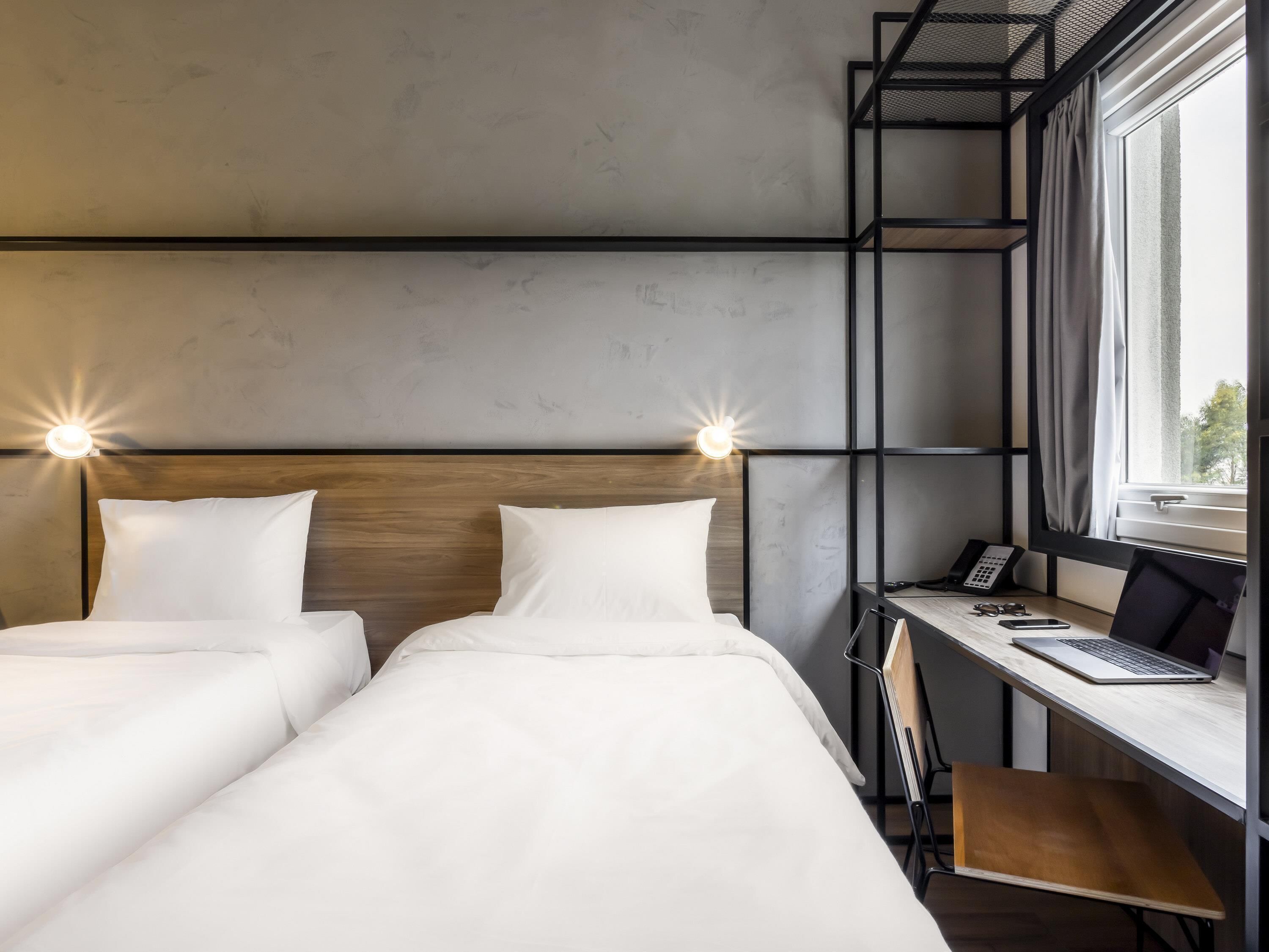 Habitación de hotel con dos camas, un escritorio, una laptop, un teléfono y una ventana con cortinas.
